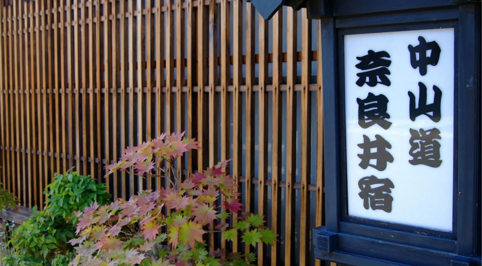 A Nakasendo road marker for Narai-juku framed by autumn maple leaves