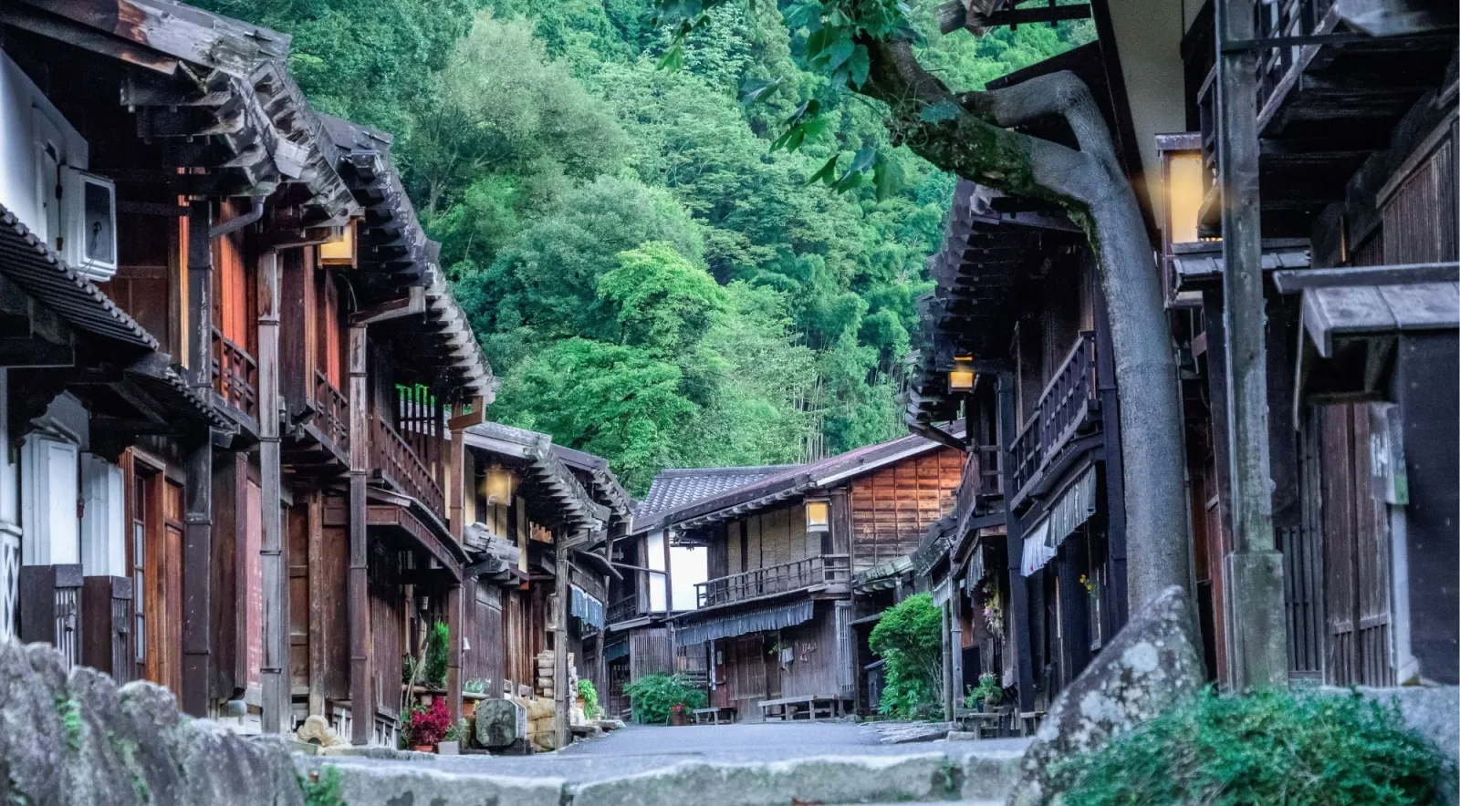 Narai-juku's lantern-lit street at dusk, framed by forested hills